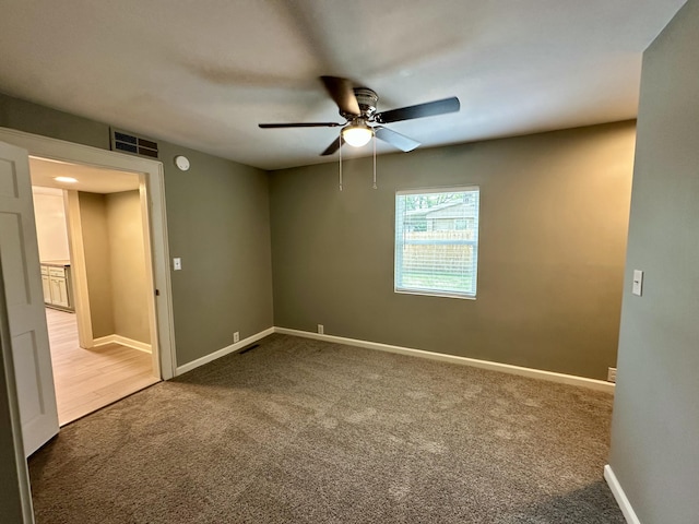 carpeted empty room featuring visible vents, a ceiling fan, and baseboards
