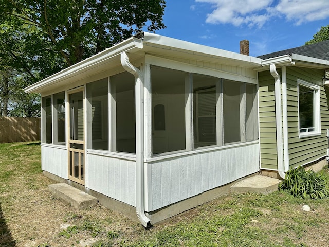 view of property exterior with fence, a chimney, and a sunroom