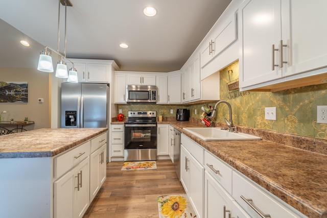 kitchen with backsplash, appliances with stainless steel finishes, light wood-type flooring, a sink, and white cabinetry