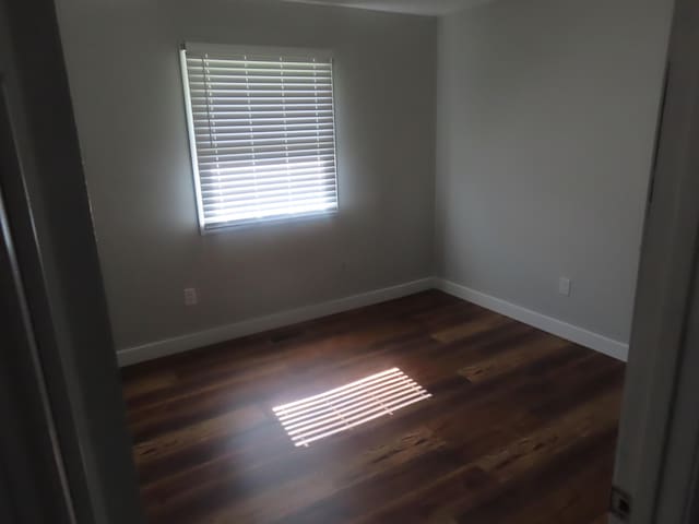 unfurnished room featuring baseboards and dark wood-style flooring