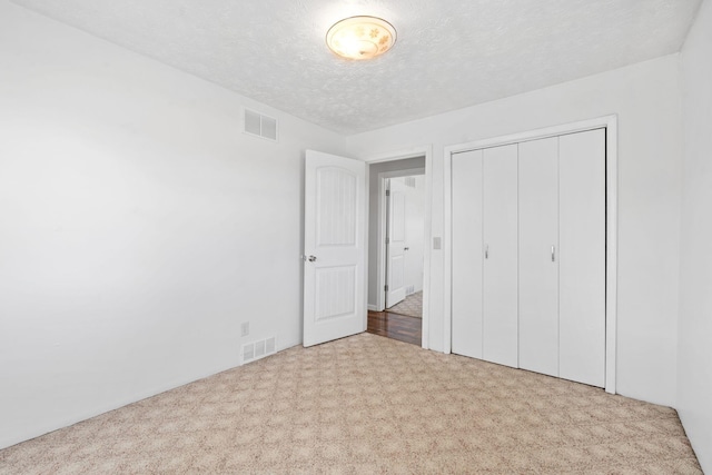 unfurnished bedroom with visible vents, carpet flooring, a textured ceiling, and a closet
