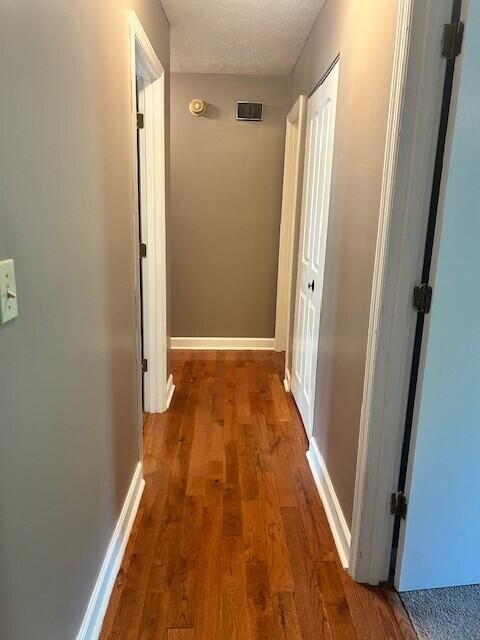 hallway featuring visible vents, baseboards, and wood finished floors