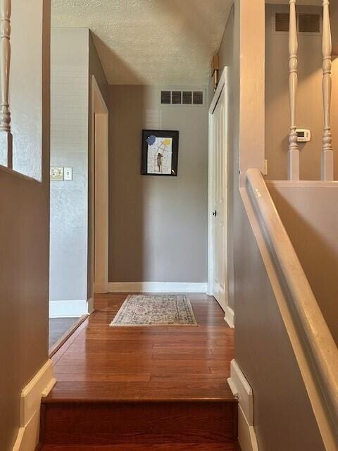 corridor with a textured ceiling, baseboards, visible vents, and hardwood / wood-style flooring