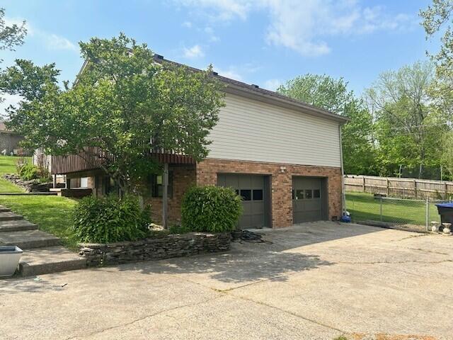 view of side of home featuring brick siding, a garage, fence, and driveway