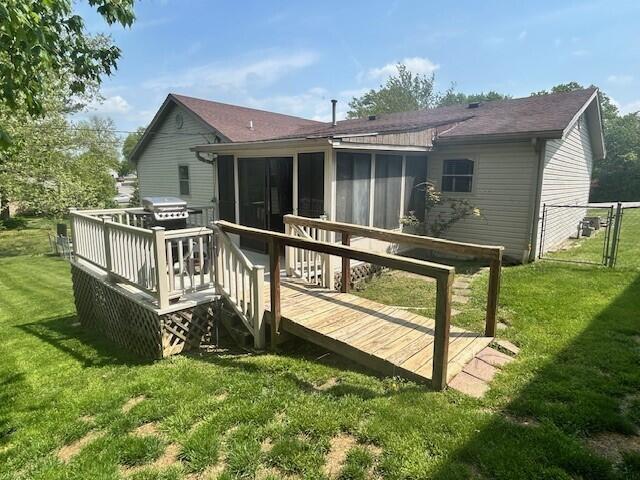 back of property with roof with shingles, a sunroom, a deck, a gate, and a yard