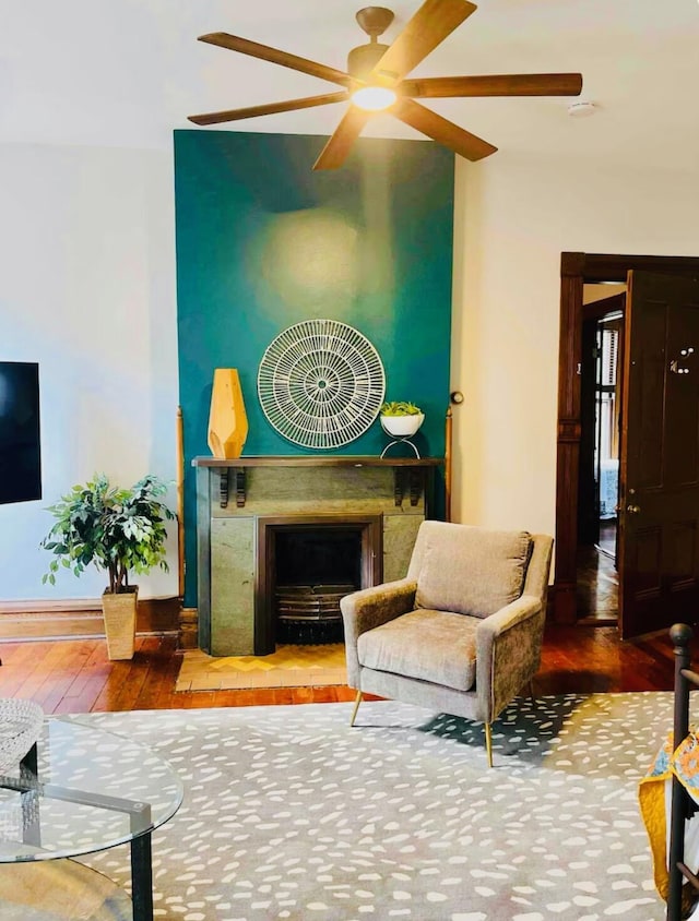 living room featuring a ceiling fan, baseboards, a fireplace with raised hearth, and hardwood / wood-style flooring