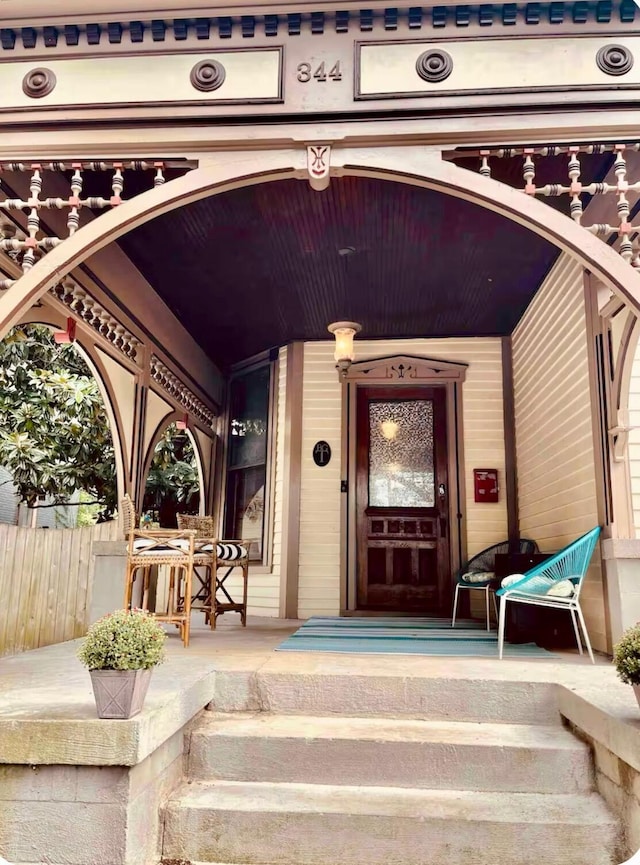 view of exterior entry with covered porch and fence