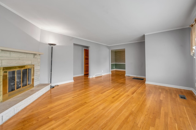 unfurnished living room with crown molding, light wood-type flooring, a stone fireplace, and visible vents