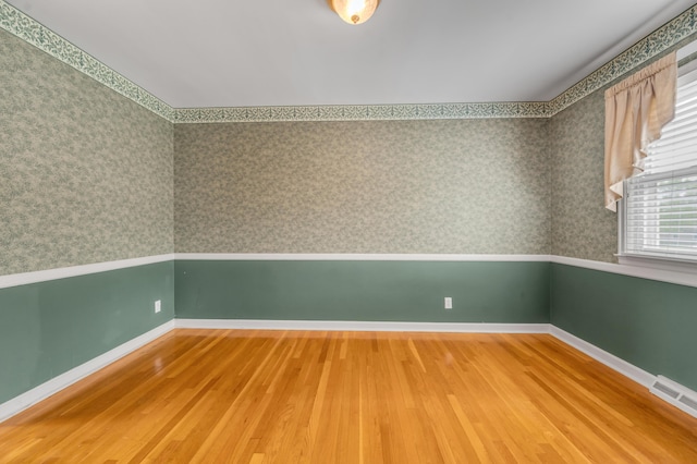 unfurnished room featuring baseboards, wallpapered walls, wood finished floors, and visible vents