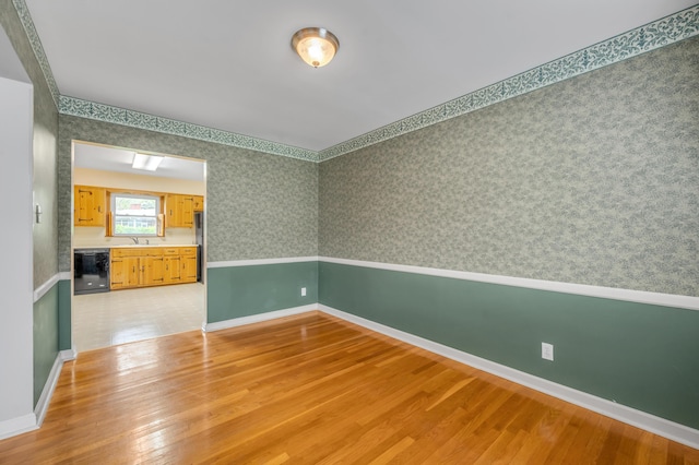 empty room featuring baseboards, wallpapered walls, a sink, and light wood-style flooring