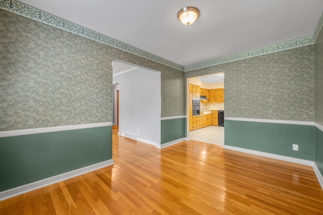 spare room with baseboards, wallpapered walls, light wood-style flooring, and visible vents