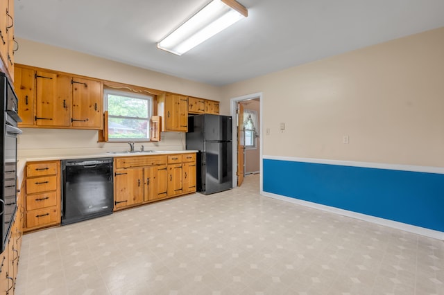 kitchen with brown cabinets, a sink, light countertops, light floors, and black appliances