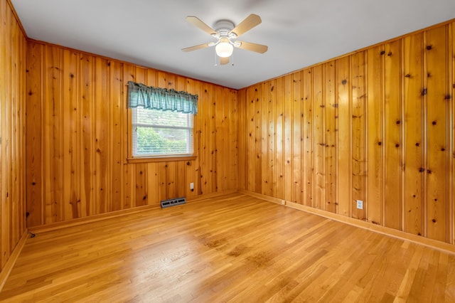 empty room featuring wooden walls, a ceiling fan, wood finished floors, and visible vents