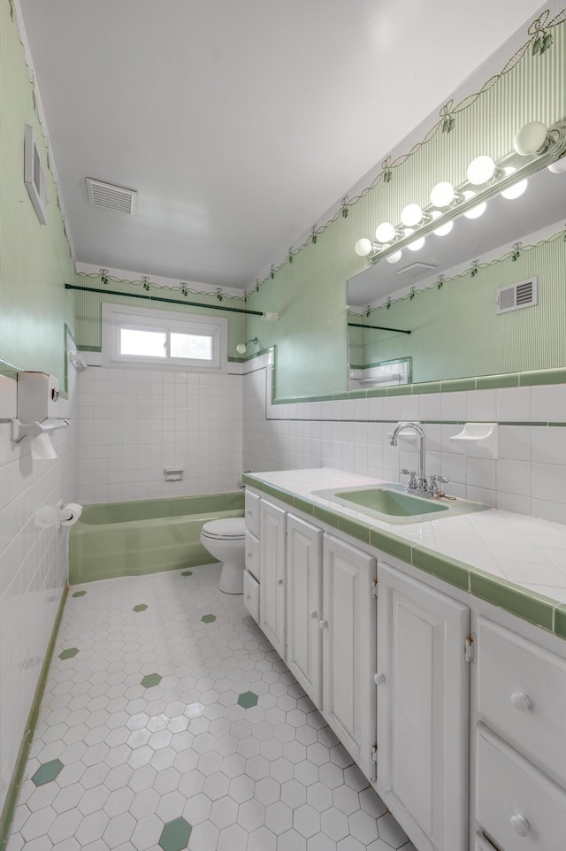 full bathroom featuring tile walls, vanity, toilet, and visible vents