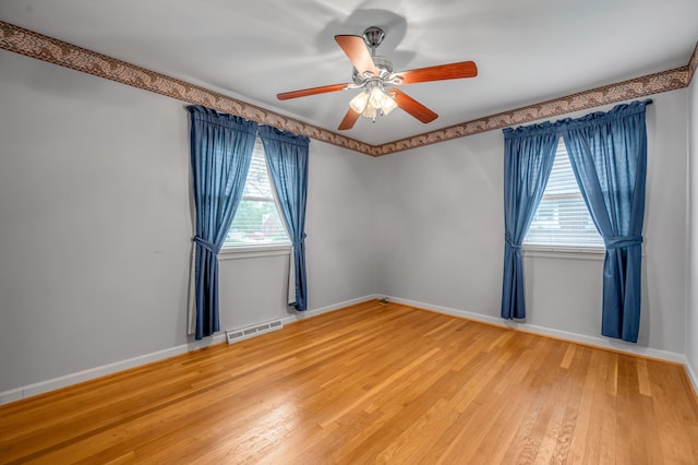 spare room featuring light wood-style floors, baseboards, a ceiling fan, and visible vents