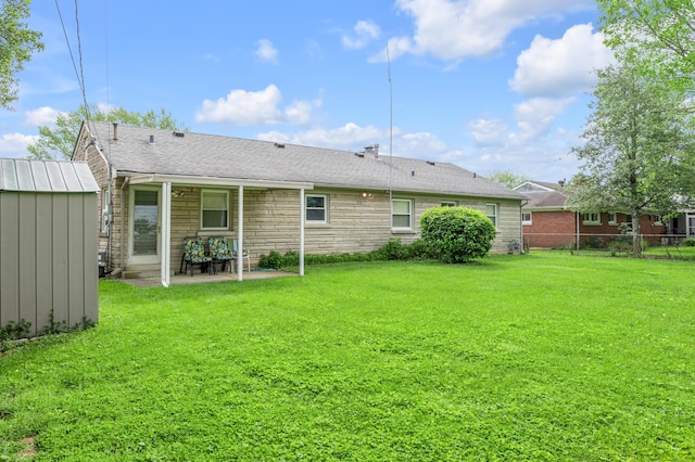 rear view of property featuring a patio, a lawn, fence, and an outbuilding