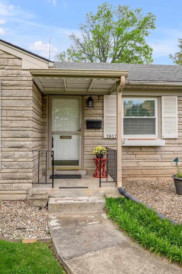 entrance to property with a shingled roof and stone siding