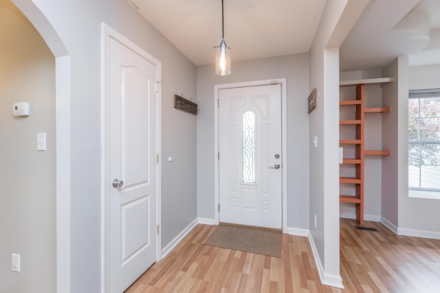 foyer with arched walkways, baseboards, visible vents, and light wood-type flooring