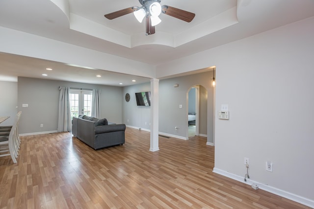unfurnished living room with arched walkways, a ceiling fan, light wood finished floors, and a raised ceiling