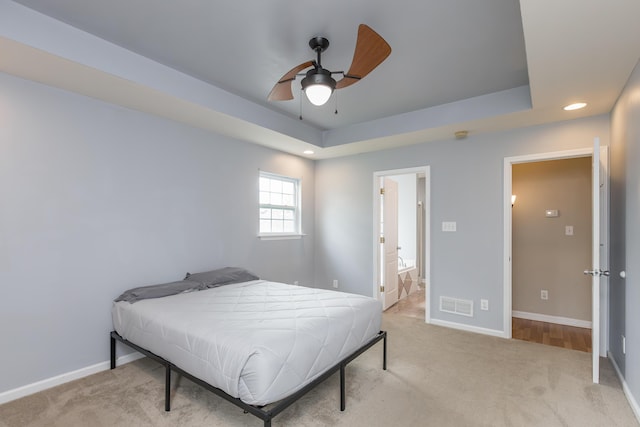 bedroom with visible vents, a raised ceiling, baseboards, and light colored carpet