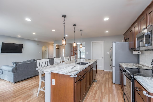 kitchen with a kitchen breakfast bar, a center island with sink, a sink, light wood-style floors, and stainless steel appliances