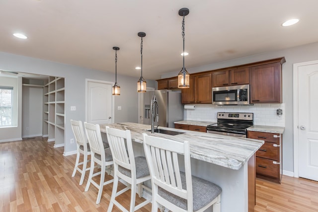 kitchen featuring backsplash, appliances with stainless steel finishes, a center island with sink, and light wood finished floors