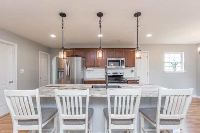 kitchen with backsplash, pendant lighting, stainless steel appliances, recessed lighting, and an island with sink