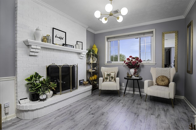 sitting room with ornamental molding, wood finished floors, a notable chandelier, and a fireplace