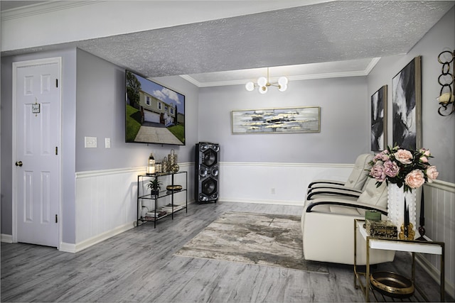 living area featuring a textured ceiling, crown molding, wood finished floors, a wainscoted wall, and a notable chandelier