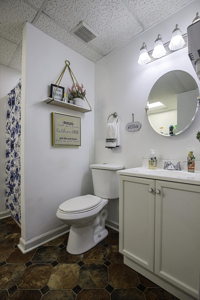 bathroom featuring visible vents, vanity, toilet, baseboards, and a drop ceiling