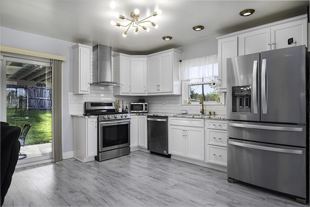 kitchen featuring light stone countertops, wall chimney exhaust hood, a chandelier, appliances with stainless steel finishes, and backsplash