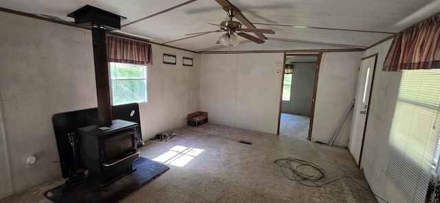 unfurnished living room featuring carpet, ceiling fan, lofted ceiling with beams, and a wood stove