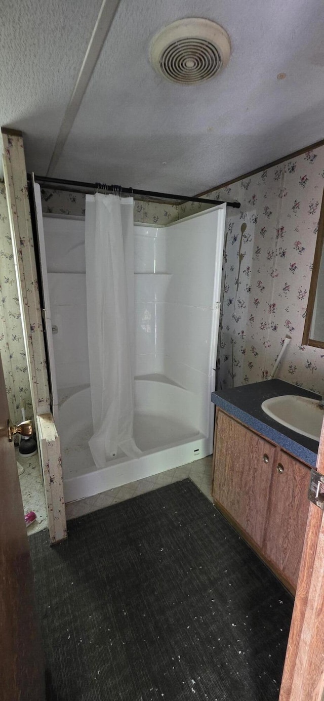full bathroom with a textured ceiling, visible vents, a shower stall, vanity, and wallpapered walls