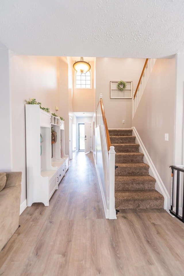 entrance foyer with a textured ceiling, baseboards, stairs, and light wood-style flooring
