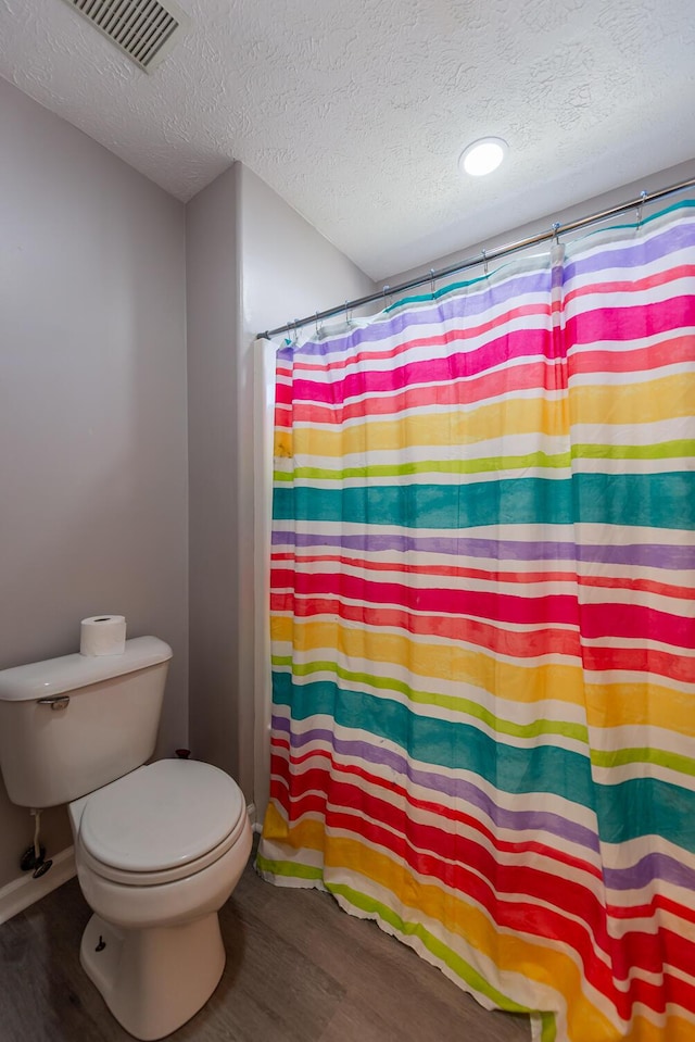 full bathroom featuring toilet, a textured ceiling, visible vents, and wood finished floors
