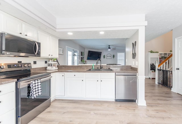 kitchen featuring appliances with stainless steel finishes, a sink, a ceiling fan, white cabinetry, and light wood-type flooring