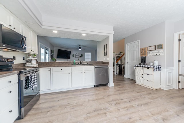 kitchen featuring ceiling fan, a sink, white cabinets, stainless steel appliances, and light wood-style flooring