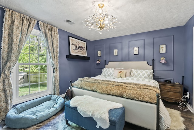 bedroom featuring dark wood-style flooring, a textured ceiling, visible vents, baseboards, and a chandelier