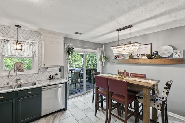 kitchen featuring backsplash, visible vents, hanging light fixtures, dishwasher, and a sink