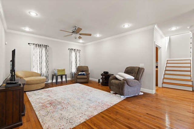 living area featuring ceiling fan, ornamental molding, light wood-style flooring, and stairway