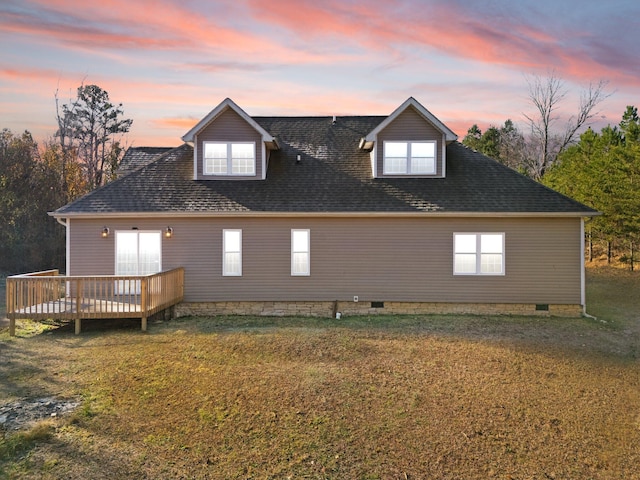 back of house at dusk featuring a lawn, a wooden deck, a shingled roof, and crawl space