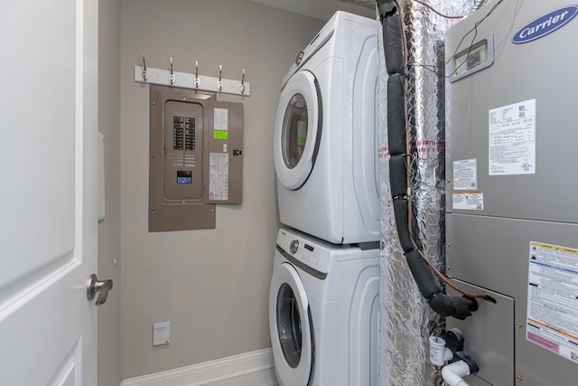 clothes washing area featuring laundry area, electric panel, stacked washer / dryer, baseboards, and heating unit