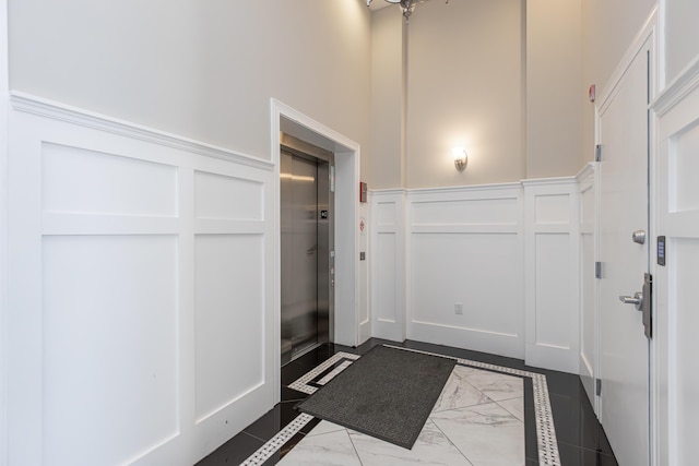 interior space with a high ceiling, wainscoting, a decorative wall, and elevator
