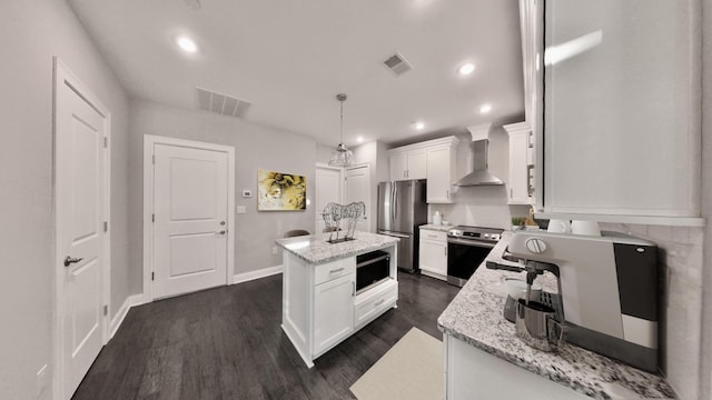 kitchen featuring visible vents, a center island, wall chimney exhaust hood, white cabinetry, and appliances with stainless steel finishes
