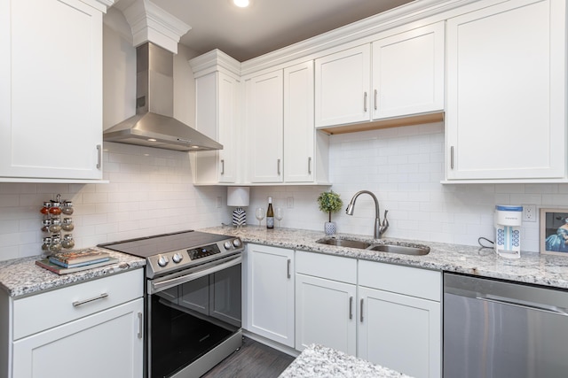 kitchen with decorative backsplash, wall chimney exhaust hood, white cabinetry, a sink, and stainless steel appliances