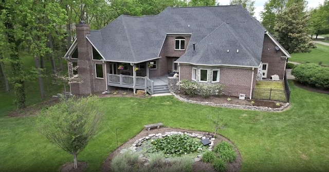 rear view of property with a wooden deck, a chimney, brick siding, a shingled roof, and a lawn