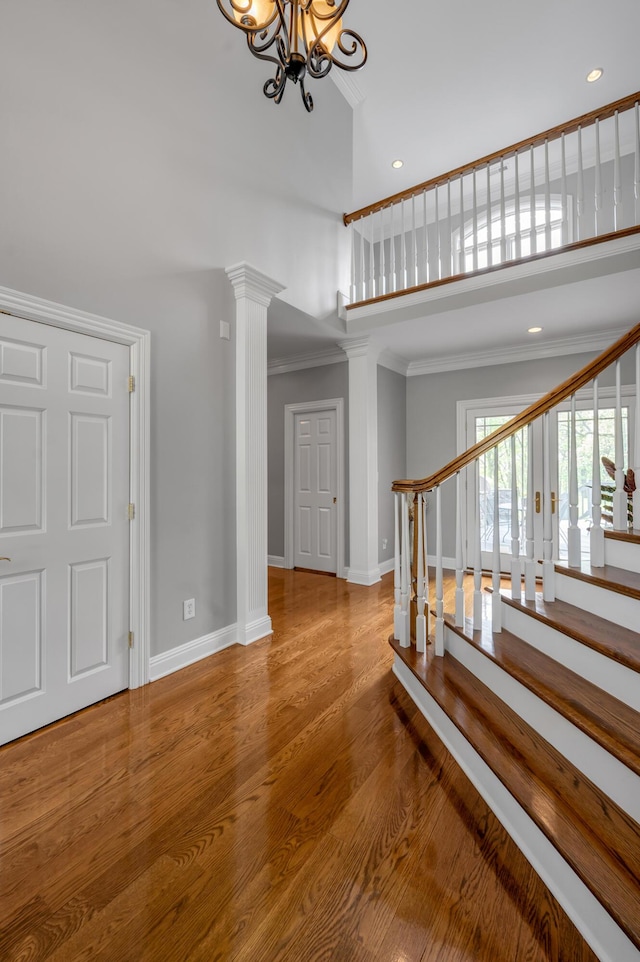 interior space with baseboards, ornamental molding, an inviting chandelier, a high ceiling, and ornate columns