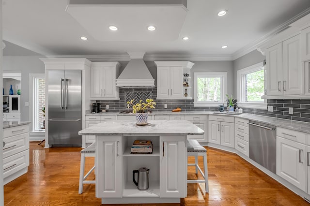 kitchen with a kitchen bar, open shelves, premium range hood, white cabinets, and stainless steel appliances