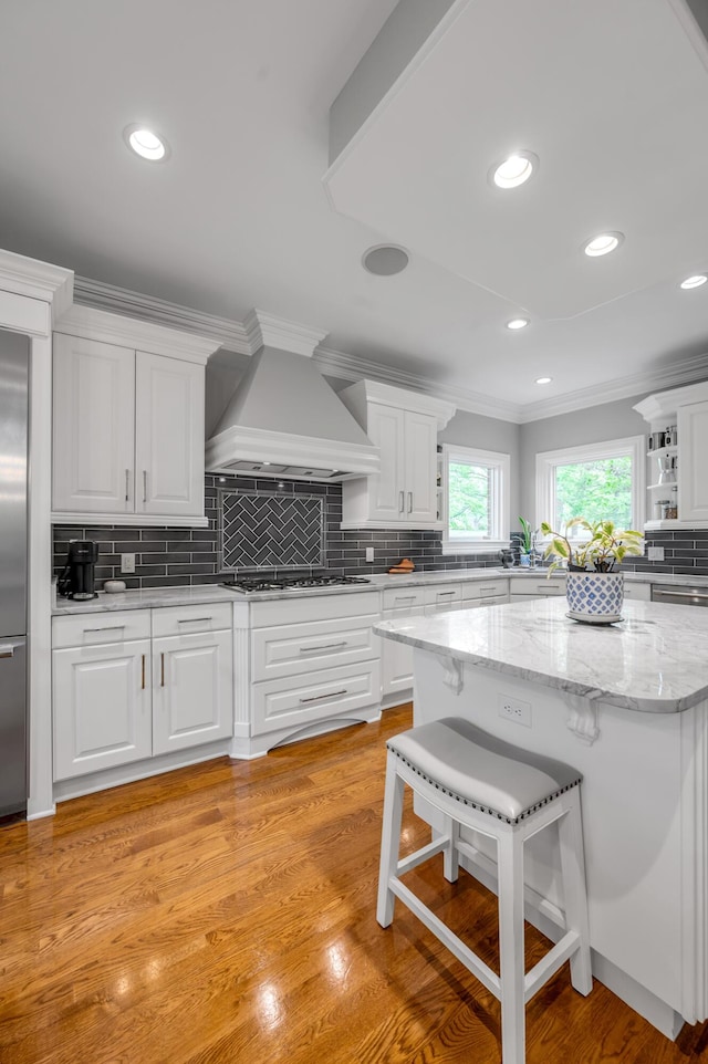 kitchen with custom range hood, decorative backsplash, white cabinetry, and appliances with stainless steel finishes