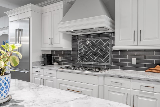 kitchen featuring white cabinets, light stone counters, premium range hood, stainless steel appliances, and tasteful backsplash